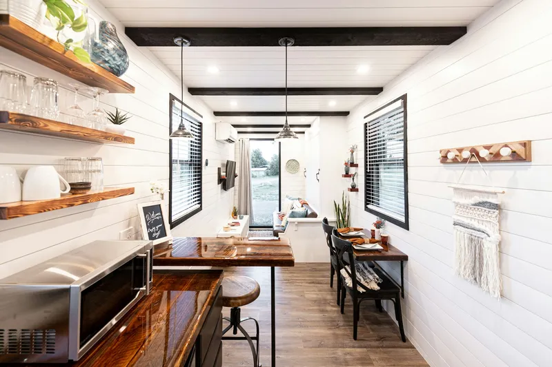 Schmale, helle Küchenzeile in einem Container-Tiny-House mit offenen Holzregalen, Theke und kleinem Esstisch