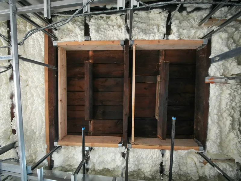 Holzbalken im Umbau, umgeben von weißer Sprühschaumdämmung und Metallprofilen
